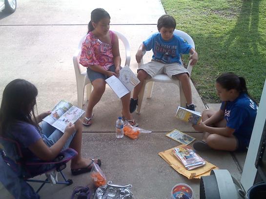 Four children sit on a porch reading comics and enjoying each other’s company.