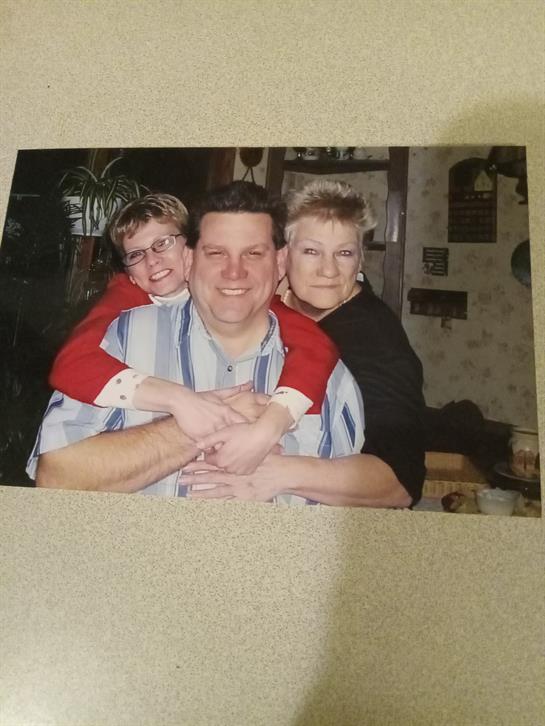 Three family members smile and embrace each other in a warm, inviting atmosphere.