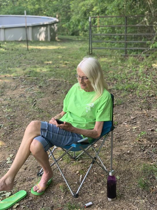 Elderly woman enjoys her time outside, engaged with her smartphone in a peaceful setting.