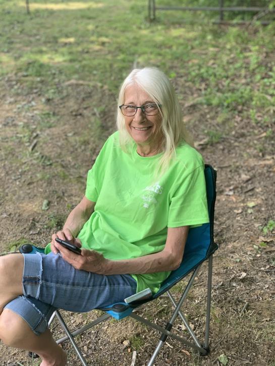 A woman with long white hair and glasses relaxes in a chair, enjoying the outdoors.