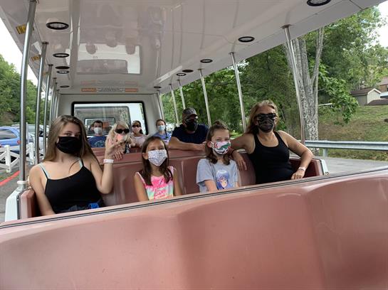 Family and friends relax together on a bus, enjoying the outdoors while wearing masks.