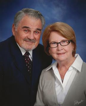 Elderly couple smiles warmly at the camera in a studio setting, radiating affection for each other.