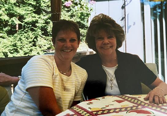 Two women are sitting together at a table in a garden, smiling and enjoying a pleasant afternoon.