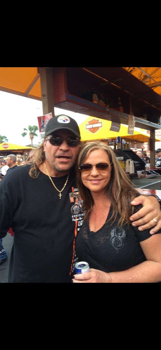 Two people pose together at a bustling motorcycle rally, enjoying the lively atmosphere.
