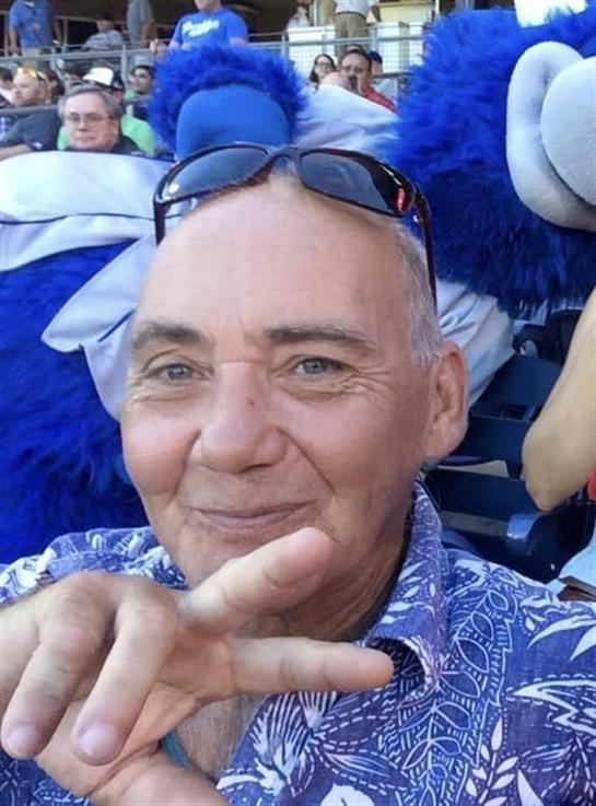A joyful man poses for a selfie, flashing a peace sign at a lively outdoor event filled with fans.