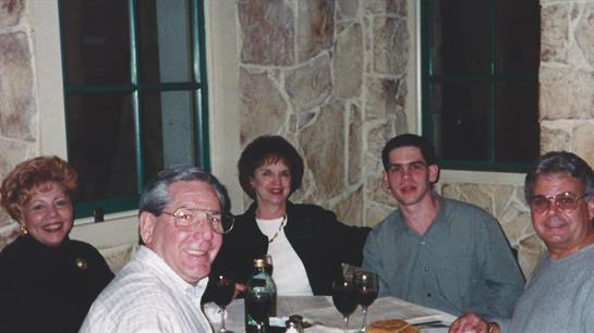 Friends and family sit together at a table, enjoying dinner and laughter in a warm setting.