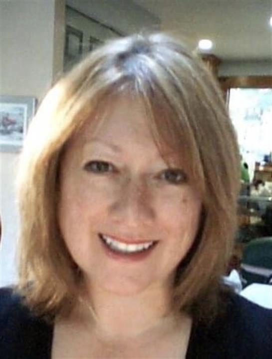 Woman with light brown hair smiles warmly in a charming indoor cafe setting, exuding friendliness.