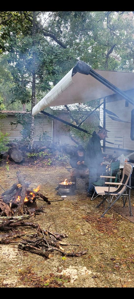 A person enjoys cooking over a campfire while relaxing at a campsite in the woods.