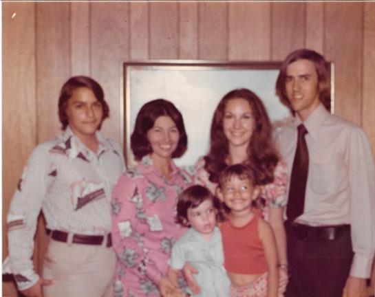 A joyful family poses together in front of a wooden wall, showcasing their outfits from the 1970s.