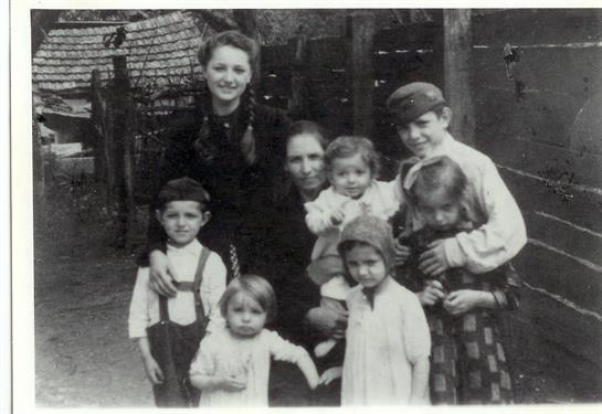 A group of children and two women are posing together outdoors in an old village.
