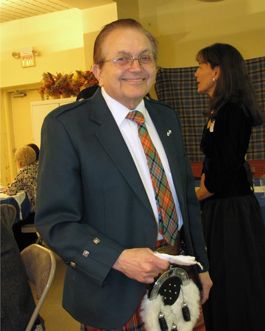 Man wearing formal attire smiles while holding a small dog at a social event indoors.