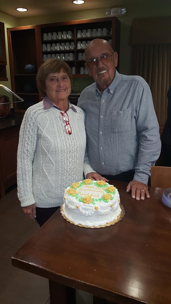 A couple stands proudly beside a beautifully decorated cake, smiling joyfully in a warm atmosphere.