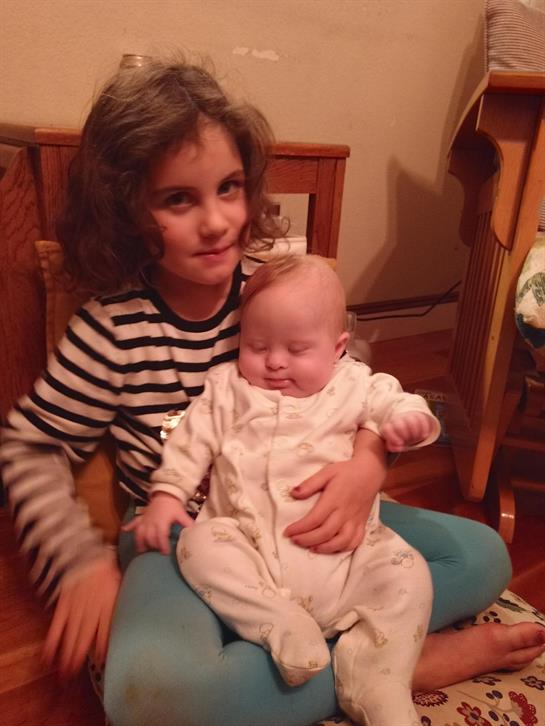 Young girl holds a baby brother on her lap, both are relaxed in a warm, inviting home atmosphere.