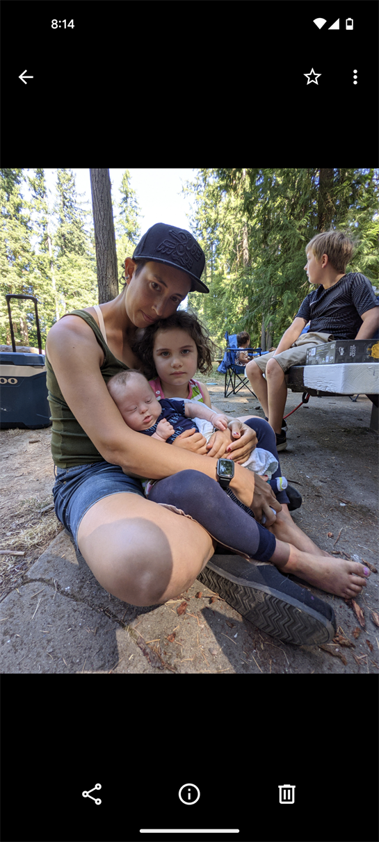 A mother enjoys time with her children, holding her baby while sitting on the forest floor.