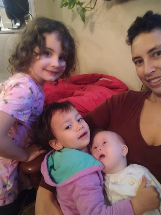 Three young children and a caregiver share a warm, joyful moment in a cozy home environment.
