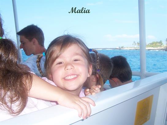 Child smiles by a boat railing, surrounded by friends in the sunny weather.
