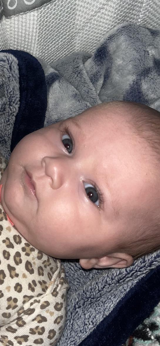 A young baby stares with curiosity, showcasing large, expressive eyes in a warm environment.