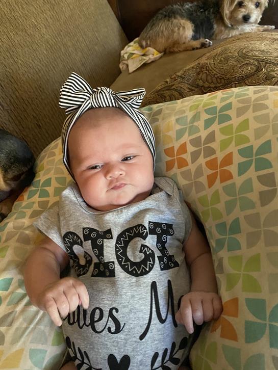 An adorable baby girl is relaxing on vibrant cushions, wearing a cute outfit and headband.