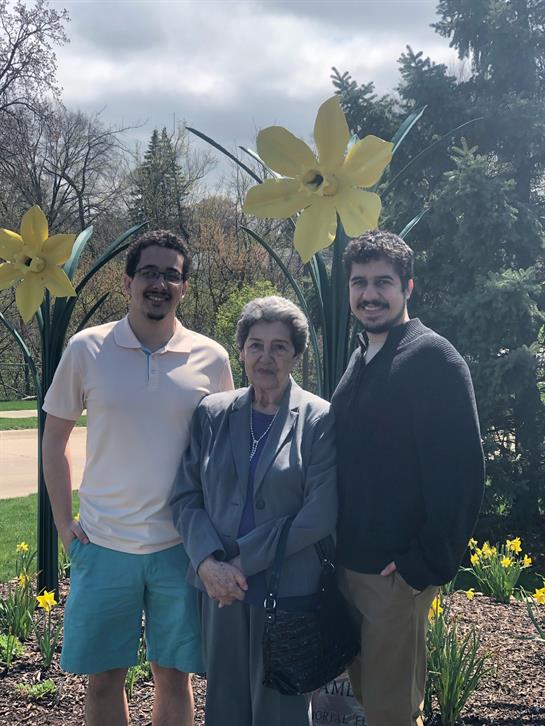Two men and a woman stand together smiling amid large yellow flowers in a garden.