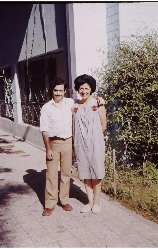 Man and woman pose happily outside a building amidst greenery, enjoying their time together.