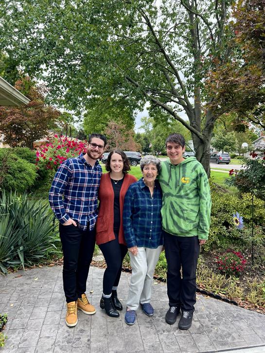 Four family members pose together outdoors surrounded by lush greenery and colorful flowers.