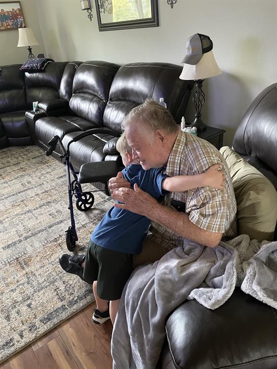 A young boy hugs his grandfather affectionately in a comfortable living space filled with love.