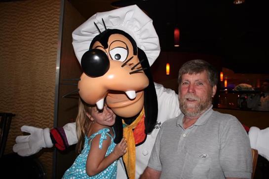 A girl hugs a chef character, smiling as a man stands nearby in a dining venue.
