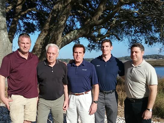 Five men enjoy a sunny day together under a large tree in a beautiful outdoor setting.