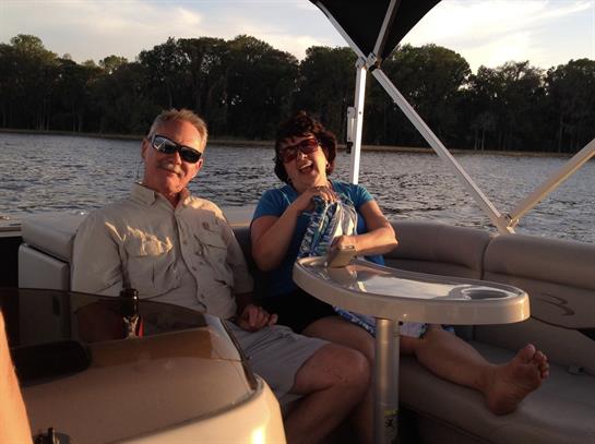 Two individuals relax on a boat, sipping drinks while enjoying a peaceful lakeside sunset.