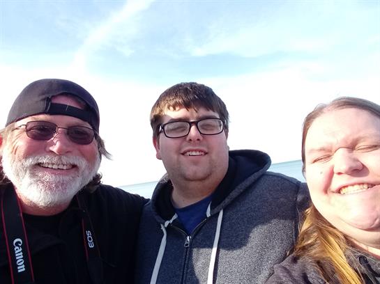 Three friends smile together at the beach on a sunny day, enjoying their time.
