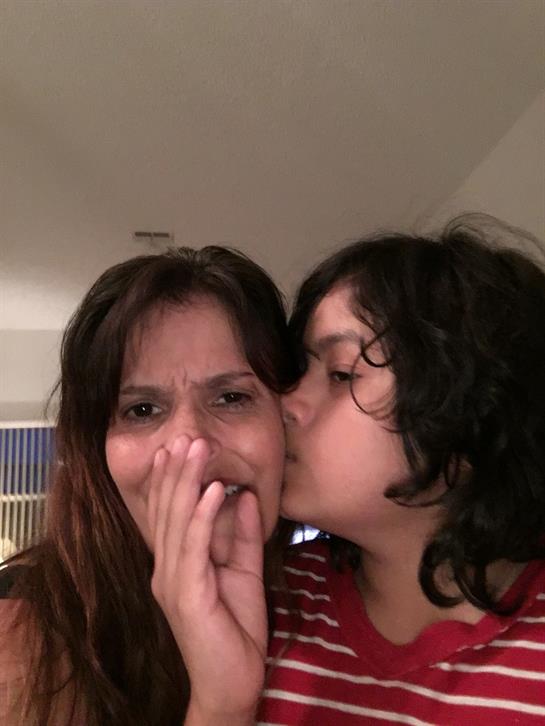 A child leans in to kiss a woman's cheek as they share a joyful moment together at home.