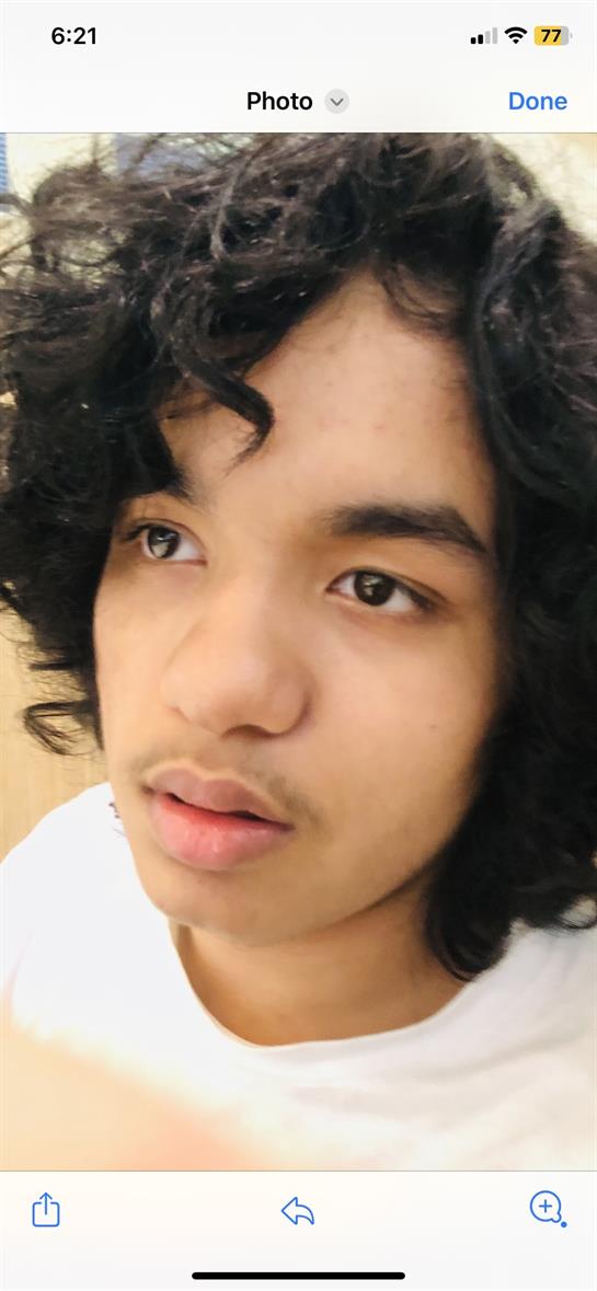 Teenager with curly hair gazes off-camera, expressing a moment of contemplation indoors.