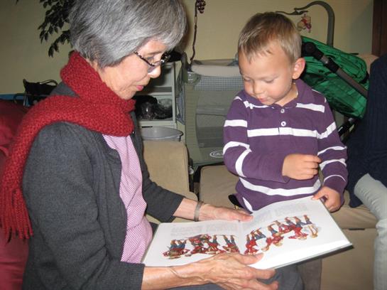 An elderly woman reads to a young boy, both engaged and enjoying a moment together indoors.