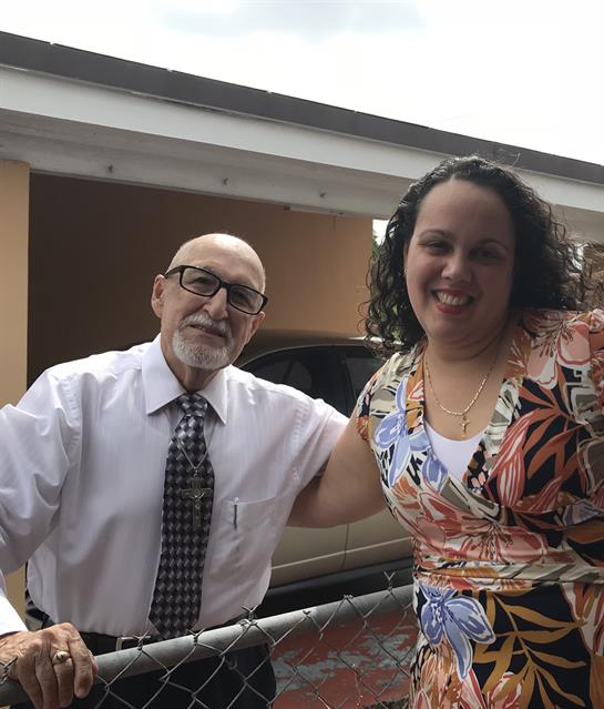 A grandfather and granddaughter share a warm embrace at a family gathering in a backyard.