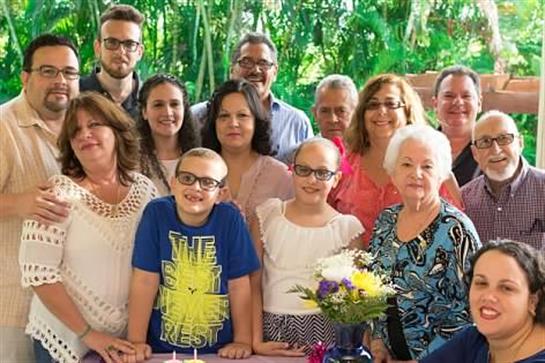 A joyful family celebrates a child's birthday outdoors among lush trees and flowers.