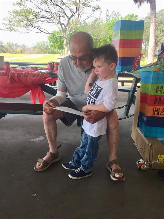 A grandfather reads to his grandson at a park picnic, filled with joy and laughter.