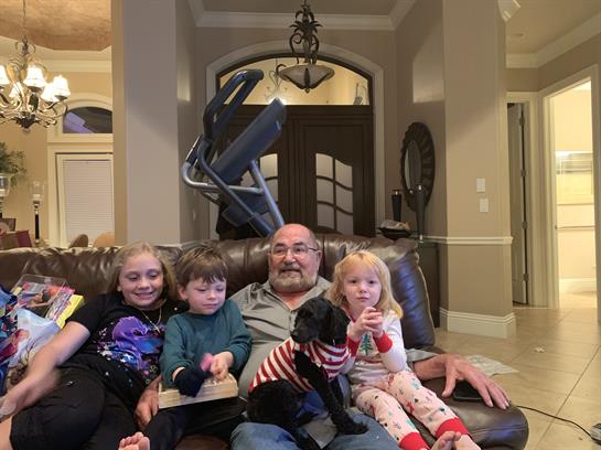 Children and a man sit together on a couch, enjoying each other's company with a dog.