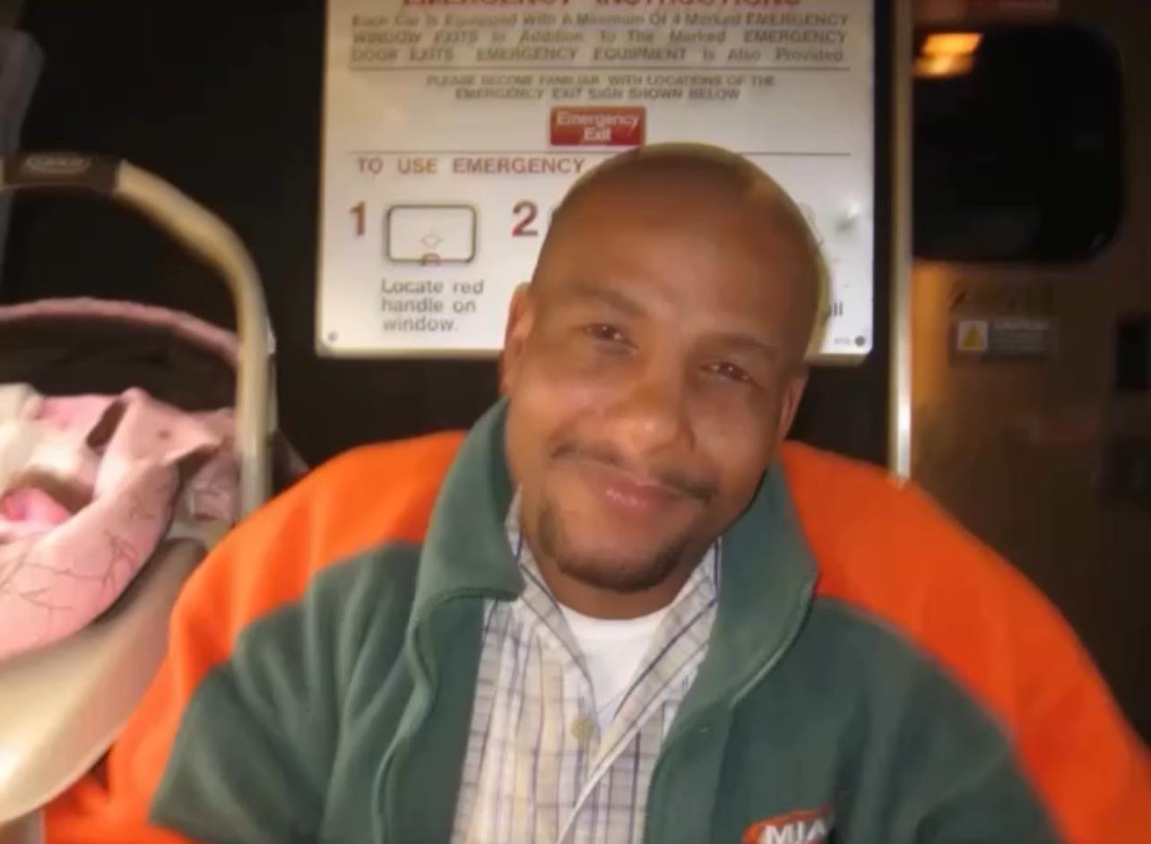 A man with a warm smile is sitting comfortably on public transport, enjoying the journey.