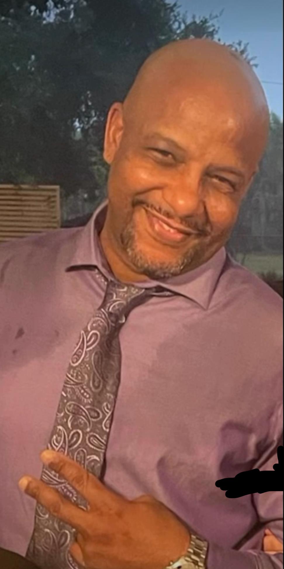 A man with a confident smile is dressed in a purple shirt and tie during a casual evening event.