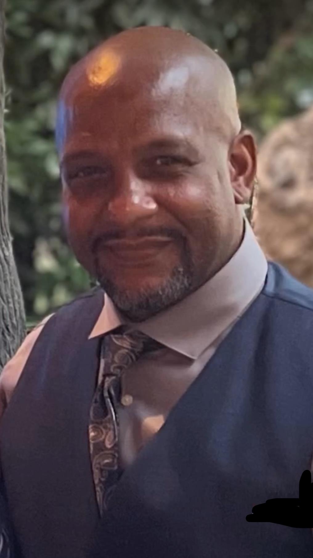 A man dressed in a suit enjoys a moment at a social event with a tree backdrop during the evening.