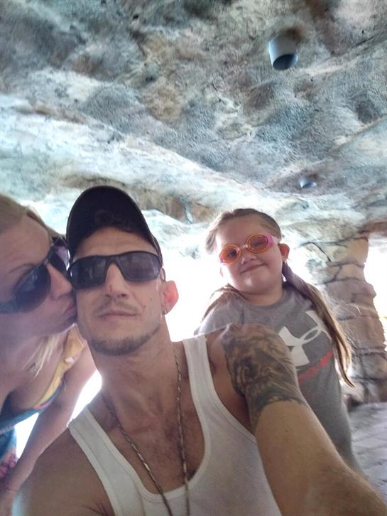 Family poses together in a cave, with one member kissing another on the cheek, all are happy.