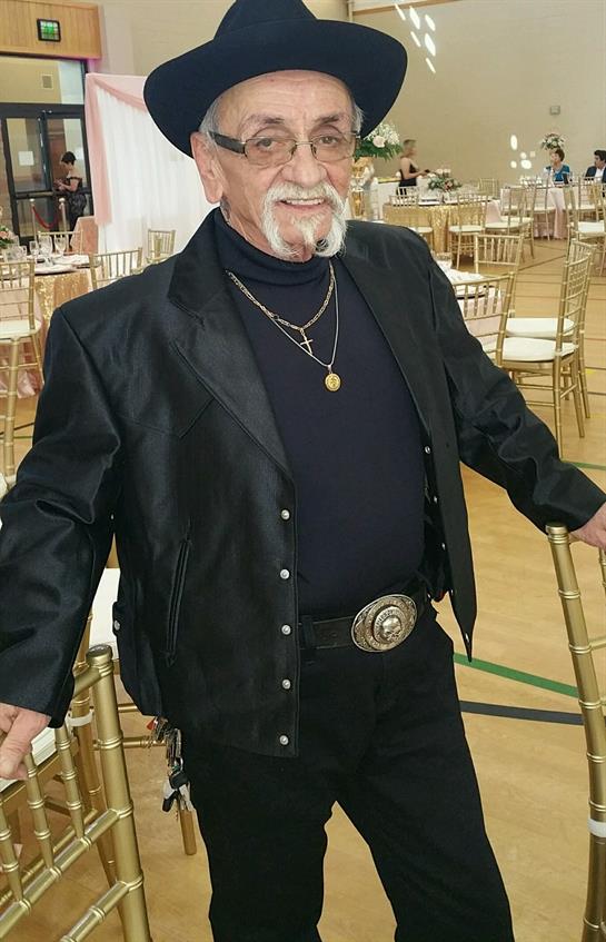 An elderly man in black stands confidently in a large hall of empty chairs.