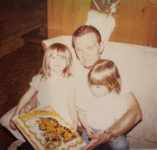 Two young girls pose with an adult man while holding a colorful dessert.