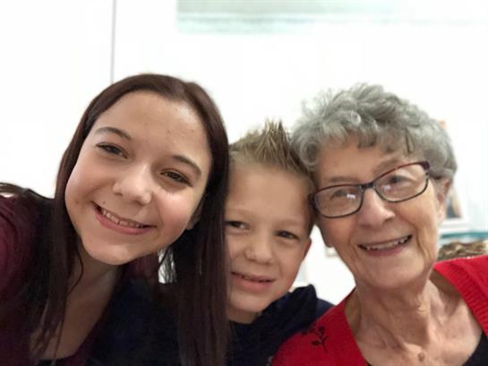 Three family members smile happily together indoors, enjoying a warm afternoon gathering.