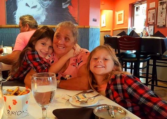 Two young girls hug an elderly woman at a restaurant while enjoying their meal together.