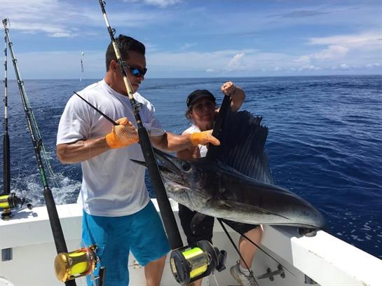 Two fishermen hold a large fish on a boat amidst beautiful ocean scenery, enjoying their adventure.