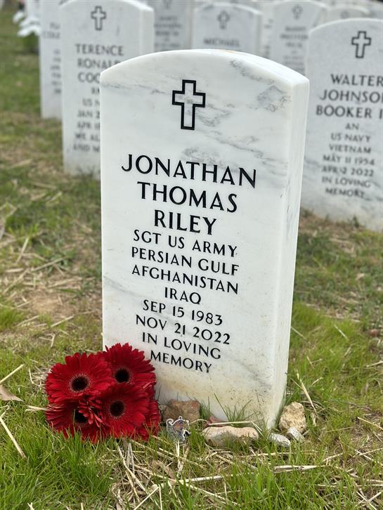 A gravestone marked with flowers commemorating Jonathan Thomas Riley, honoring his service.