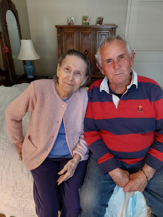 Elderly couple poses together in a cozy living room, sharing a joyful moment with family.