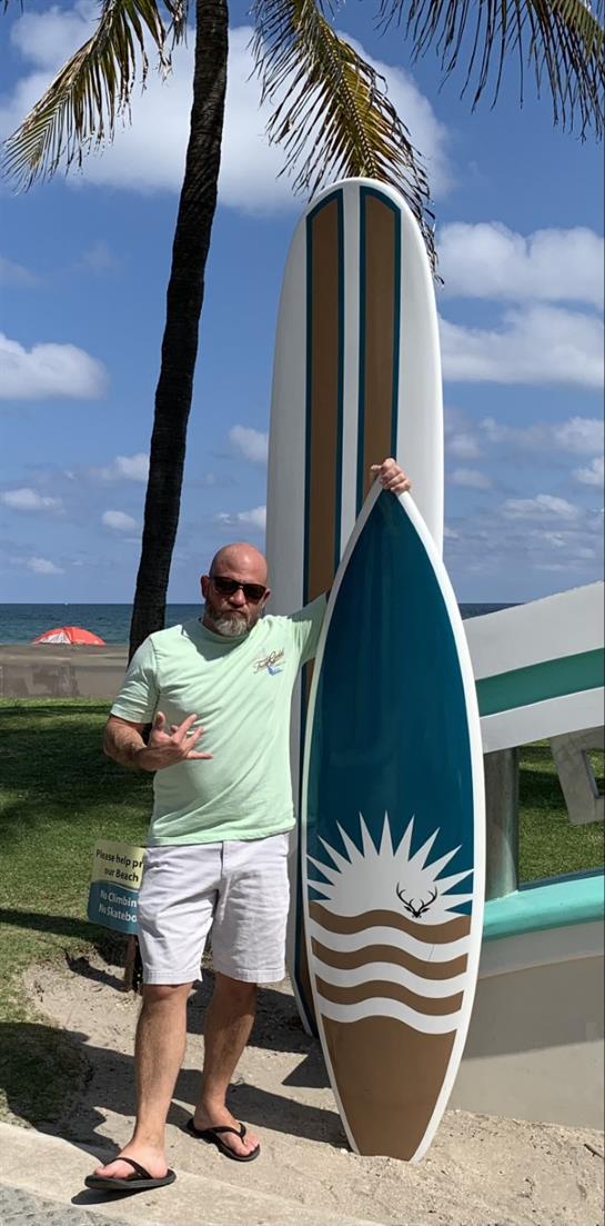 A man stands beside a vibrant surfboard while enjoying a sunny beach day near the ocean.