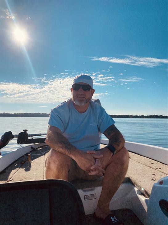 A man relaxes on a boat under a blue sky, enjoying a sunny day on the lake.